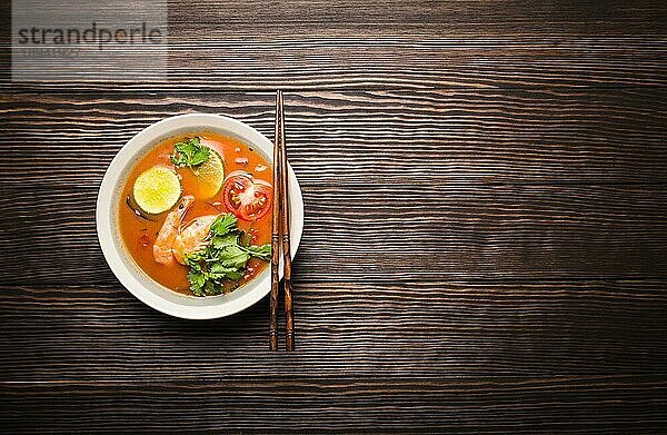 Heiße frische würzige traditionelle thailändische Suppe Tom Yum mit Garnelen in einer Schüssel auf rustikalem Holzhintergrund mit Platz für Text  Ansicht von oben. Authentische schweißtreibende und saure asiatische Suppe  beliebt in Südostasien