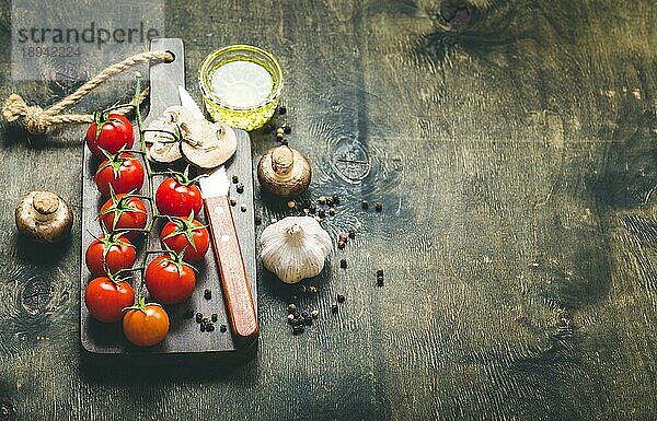 Kirschtomaten  Champignons auf Holzbrett  Messer. Mit Knoblauch  Olivenöl. Kochender Hintergrund. Platz für Text. Rohe Zutaten zum Kochen. Essen kochen. Selektiver Fokus. Lebensmittel-Hintergrund