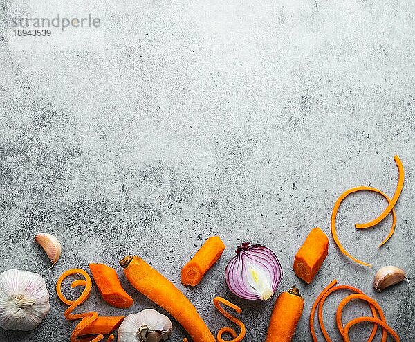 Lebensmittel Hintergrund mit freiem Raum für Text. Nahaufnahme  Draufsicht auf geschnittene frische rohe Karotte  Zwiebeln  Knoblauch auf rustikalem grauen Stein Hintergrund  Kochen  vegetarisches Essen oder gesunde Ernährung Konzept