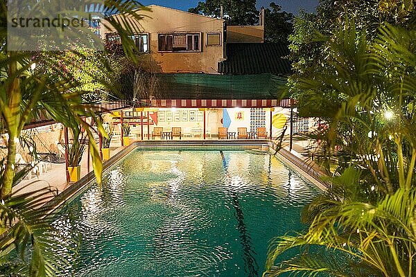 Hotelpool im Freien im Garten eines Hotels mit tropischer Vegetation mitten in Bangkok bei Nacht