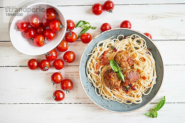 Nahaufnahme von leckeren Spaghetti mit Fleischbällchen und Tomatensauce auf einem Teller. Serviert auf einem weißen  rustikalen Holztisch. Ein italienisch-amerikanisches Gericht. Ansicht von oben. Selektiver Fokus