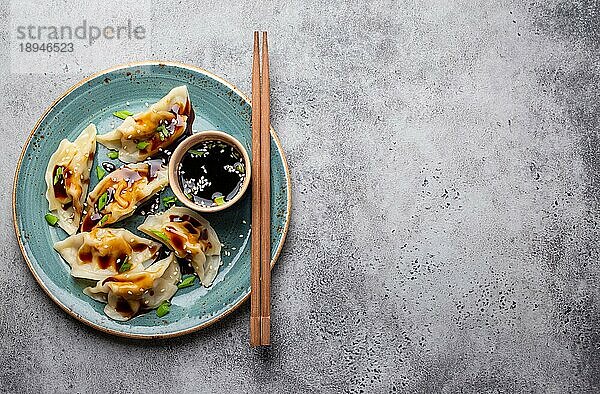Nahaufnahme  Draufsicht auf traditionelle asiatische Teigtaschen auf blauem Teller mit Sojasauce und Essstäbchen auf grauem  rustikalem Steinhintergrund mit Platz für Text. Authentische chinesische Küche  Platz zum Kopieren