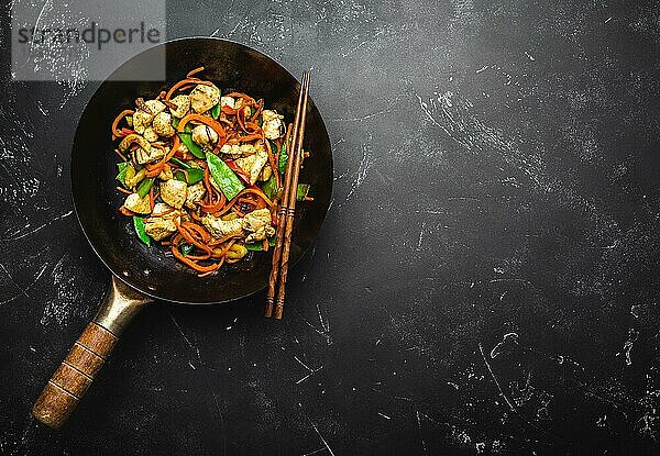 Gebratenes Huhn mit Gemüse in einer alten  rustikalen Wokpfanne  Stäbchen auf schwarzem Steinhintergrund  Nahaufnahme  Draufsicht. Traditionelle asiatische/thailändische Mahlzeit  Platz für Text