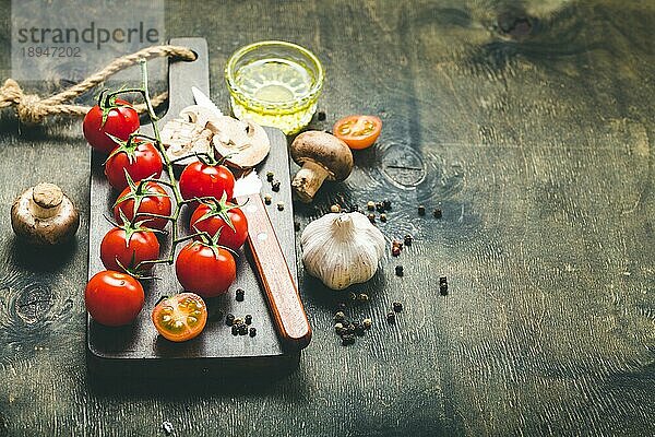 Kirschtomaten  Champignons auf Holzbrett  Messer. Mit Knoblauch  Olivenöl. Kochender Hintergrund. Platz für Text. Rohe Zutaten zum Kochen. Essen kochen. Selektiver Fokus. Lebensmittel-Hintergrund