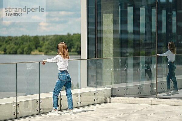 Unbekannte Frau steht auf der Aussichtsplattform  stützt sich auf das Glasgeländer und schaut auf das Wasser