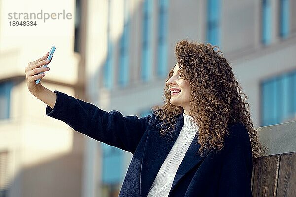 Glückliche junge Frau macht Selfie vor ihrer neuen Wohnung