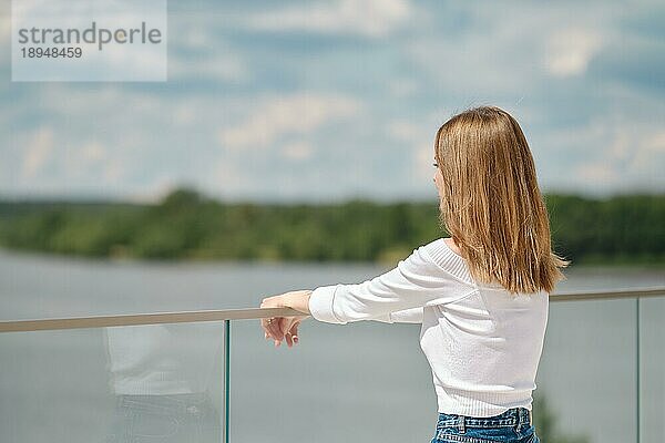 Unerkennbare Frau lehnt an einem Glasgeländer auf der Aussichtsplattform und schaut auf das Wasser