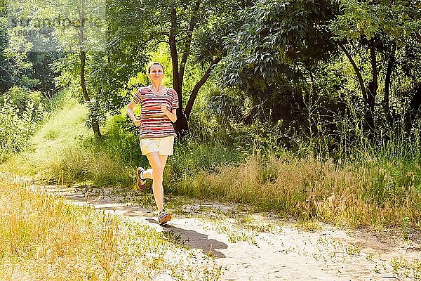 Eine glückliche ältere Frau läuft an einem warmen Sommertag im Wald mit der Sonne im Gegenlicht in Richtung des Schattens