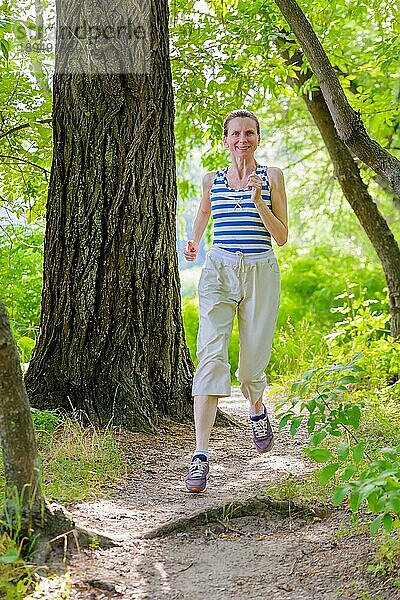 Eine glückliche ältere Frau läuft an einem warmen Sommertag im Wald in der Nähe des Sees
