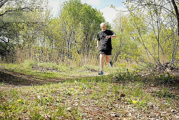 Ein älterer  schwarz gekleideter Mann läuft an einem warmen Frühlingstag durch den Wald und schaut auf Zeit seiner Stoppuhr
