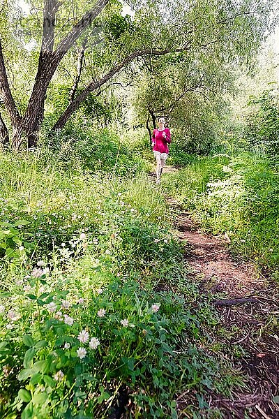 Eine glückliche ältere Frau läuft an einem warmen Sommertag im Wald auf die Natur zu