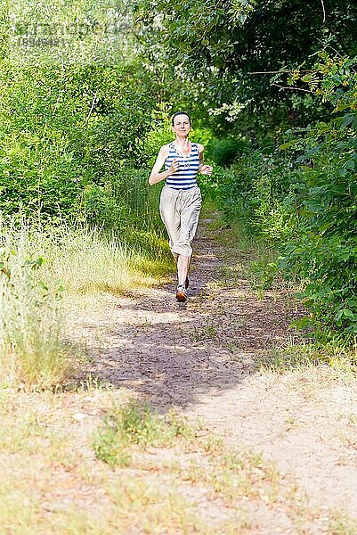 Eine glückliche ältere Frau läuft an einem warmen Sommertag im Wald