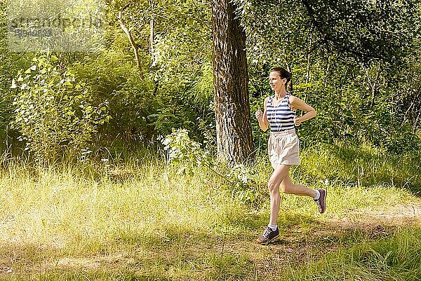 Eine glückliche ältere Frau läuft an einem warmen Sommertag im Wald dem Licht entgegen