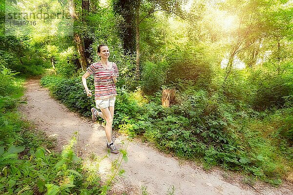Eine glückliche ältere Frau läuft an einem warmen Sommertag im Wald dem Licht entgegen