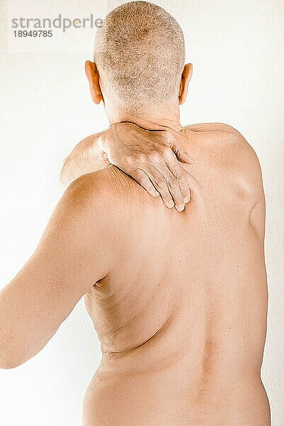 Mann massiert seinen oberen Rücken  den Trapezmuskel  wegen Schmerzen im Brustwirbelbereich aufgrund einer Verschiebung eines Rückenwirbels  der auf einen Nerv reibt