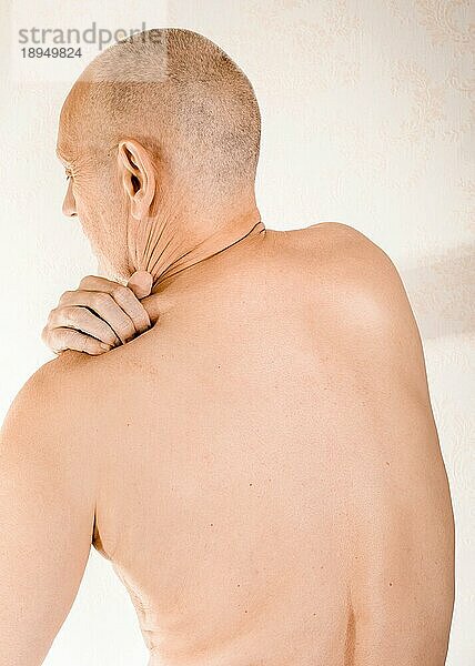 Mann massiert seinen oberen Rücken  den Trapezmuskel  wegen Schmerzen im Brustwirbelbereich aufgrund einer Verschiebung eines Rückenwirbels  der auf einen Nerv reibt