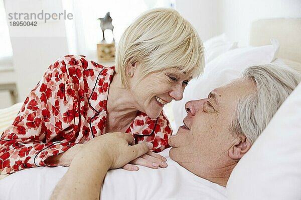 Älteres Paar liegt zusammen im Bett im Schlafzimmer und lacht sich verliebt an  Köln  Nordrhein-Westfalen  Deutschland  Europa