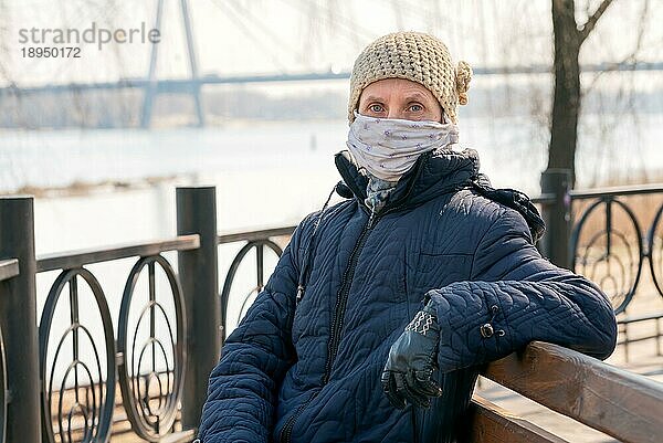 Eine arme ältere Frau trägt eine selbst gebastelte Maske  um sich vor Viren wie dem Coronavirus  auch bekannt als Covid19 oder SARS und MERS zu schützen. Sie sitzt auf einer Bank in der Nähe des Flusses