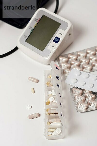 Tägliche Pillendose mit Blutdruckmessgerät im Hintergrund vor weißem Hintergrund