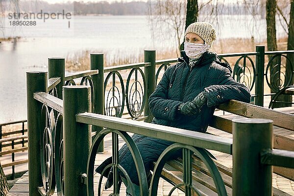 Eine arme ältere Frau trägt eine selbst gebastelte Maske  um sich vor Viren wie dem Coronavirus  auch bekannt als Covid19 oder SARS und MERS zu schützen. Sie sitzt auf einer Bank in der Nähe des Flusses