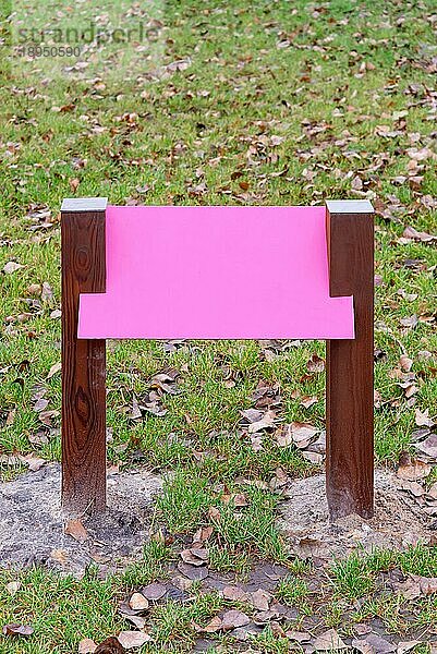 Leere rosa Holztafel für Informationen und Hinweise im Park  mit einem Hintergrund aus grünem Gras  das von Herbstblättern bedeckt ist