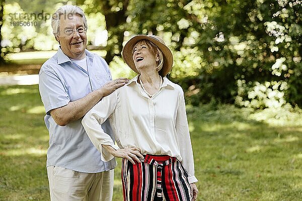 Deutschland  ein älteres  sommerlich gekleidetes Paar lacht sich im Park gegenseitig an  Europa