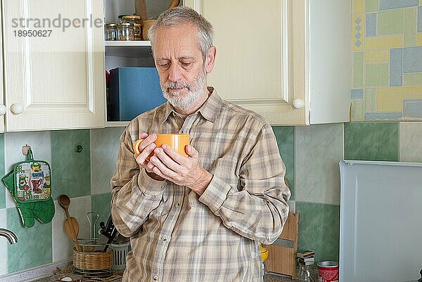 Reifer Mann trinkt seinen Kaffee in einer orangefarbenen Tasse  am Morgen in der Küche