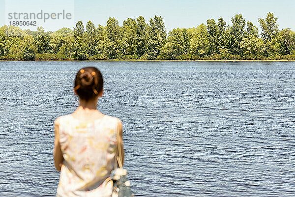 Eine Frau mit Dutt steht in der Nähe des Flusses Dnjepr in Kiew  Ukraine  und beobachtet die Bäume in der Ferne. Die Silhouette der Frau ist unscharf  vor einem fokussierten Hintergrund  Europa
