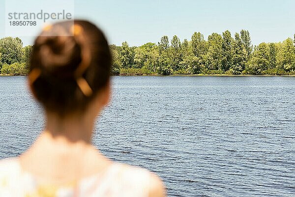 Eine Frau mit Dutt steht in der Nähe des Flusses Dnjepr in Kiew  Ukraine  und beobachtet die Bäume in der Ferne. Die Silhouette der Frau ist unscharf  vor einem fokussierten Hintergrund  Europa