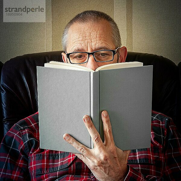 Ein älterer Mann mit Bart und Brille  der auf dem Sofa sitzt und ein Buch liest