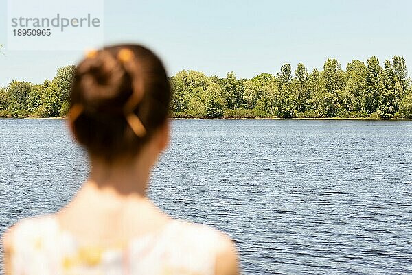 Eine Frau mit Dutt steht in der Nähe des Flusses Dnjepr in Kiew  Ukraine  und beobachtet die Bäume in der Ferne. Die Silhouette der Frau ist unscharf  vor einem fokussierten Hintergrund  Europa