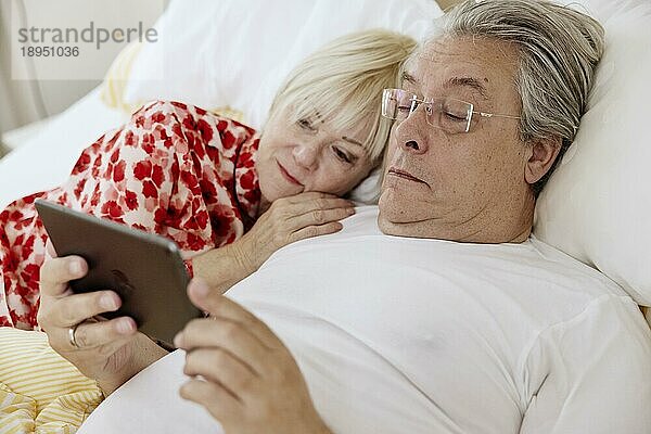 Älteres Paar liegt zusammen im Schlafzimmer im Bett und schauen zusammen auf ein Smartphone  Köln  Nordrhein-Westfalen  Deutschland  Europa