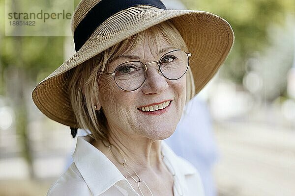 Fröhliche  lächelnde  ältere  sommerlich gekleidete Frau mit Strohhut  Brille und Perlenkette  Porträt  Köln  Nordrhein-Westfalen  Deutschland  Europa