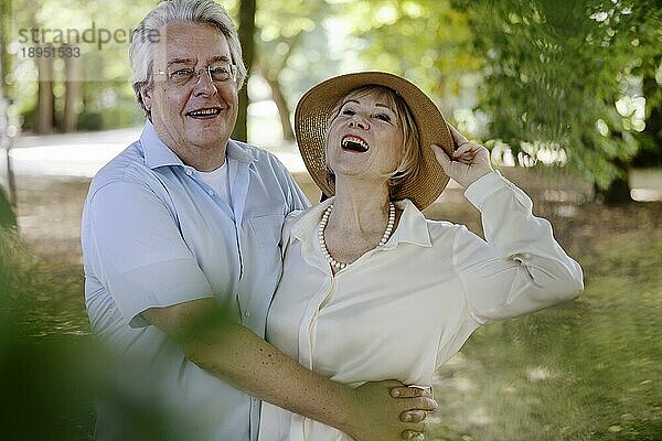 Sommerlich gekleidete Frau mit Strohhut zusammen mit ihrem Mann lachend im Park  Porträt  Köln  Nordrhein-Westfalen  Deutschland  Europa