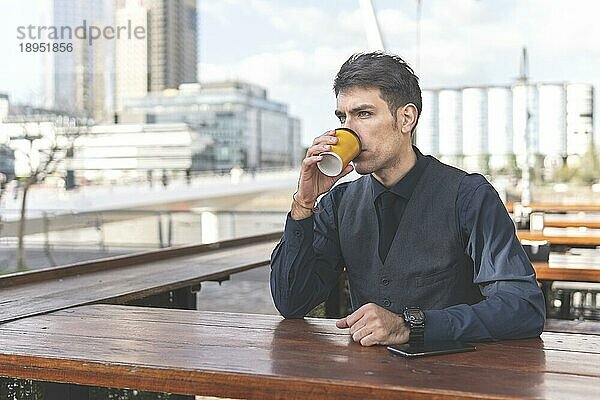 Geschäftsmann sitzt an einer Bar im Freien und trinkt einen Kaffee