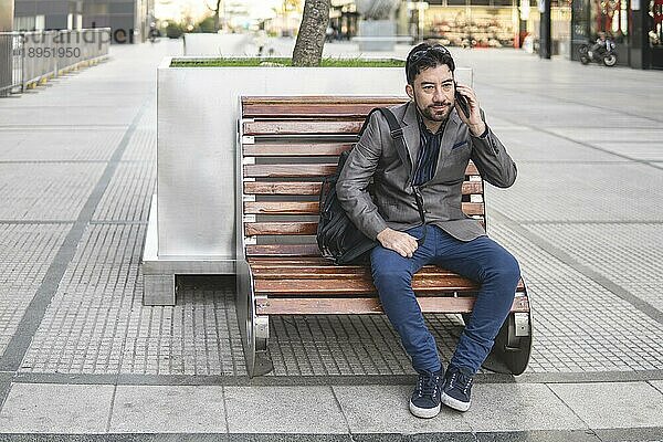 Latino Geschäftsmann  der auf einer Bank sitzt und telefoniert