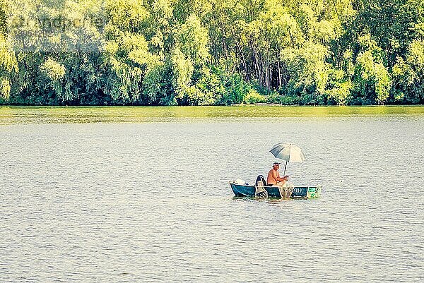 Kiew  Ukraine  25. August 2015  Ein Mann  ein Fischer  auf einem Boot auf dem Fluss Dnjepr in Kiew. Er benutzt einen Regenschirm  um sich beim Fischen vor der warmen Sommersonne zu schützen  Europa