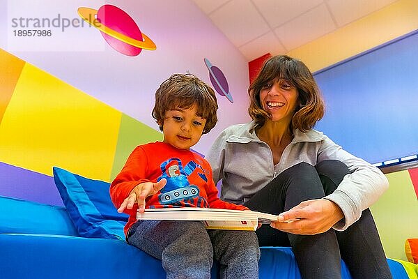 Erzieherin spielt mit einem Kind  das ein Buch liest und Spaß hat  Innenansicht eines Kindergartens