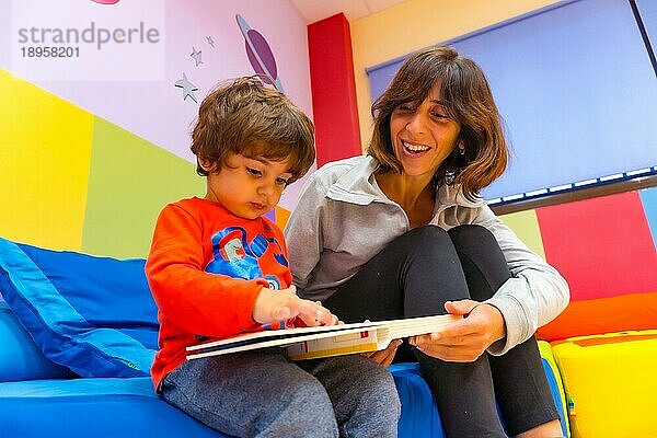 Lehrerin spielt mit einem Kind  das ein Buch liest und Spaß hat  Innenraum eines Kindergartens
