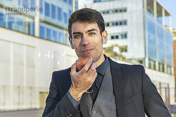 Ein attraktiver Geschäftsmann isst gerade einen Apfel auf der Straße in der Nähe seines Büros