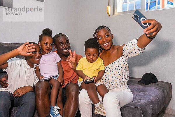 Schwarzafrikanische Familie mit ihren Kindern auf dem Sofa zu Hause  die ein Selfie mit ihrem Handy machen