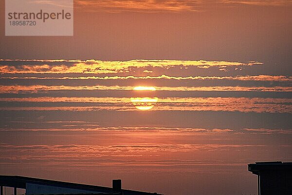 Roter Sonnenuntergang über Dachsilhouetten am späten Abend mit Wolken  die die Sonne verdecken