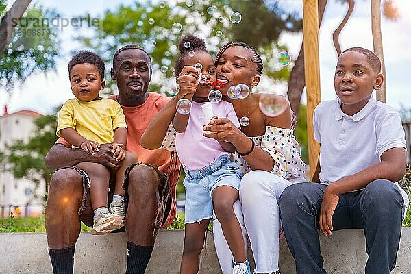 Afrikanische schwarze ethnische Familie mit Kindern auf dem Spielplatz  die neben den Bäumen im Park Seifenblasen blasen