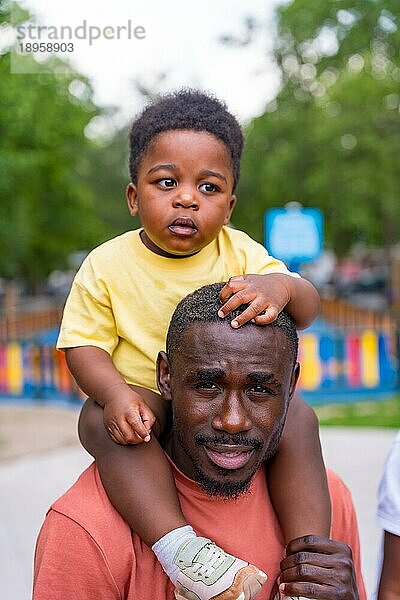 Porträt eines schwarzafrikanischen Vaters mit seinen Kindern auf dem Spielplatz des Stadtparks