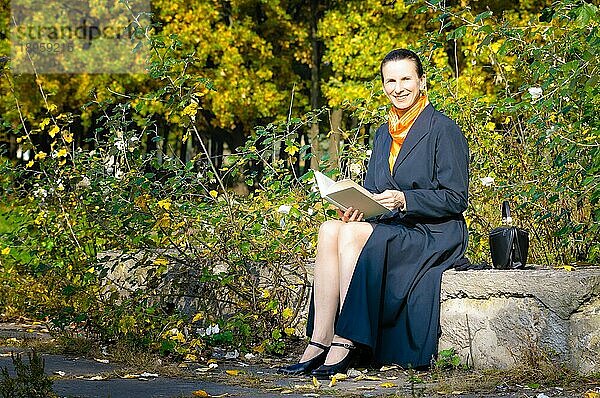 Sexy ältere Frau liest ein Buch im Park an einem sonnigen Herbsttag