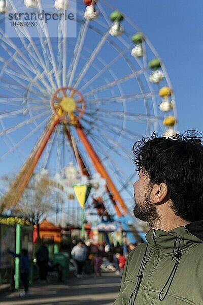 Porträt eines Latinomannes in einem Vergnügungspark  der glücklich mit dem Riesenrad im Hintergrund posiert