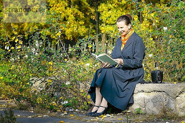 Sexy ältere Frau liest ein Buch im Park an einem sonnigen Herbsttag