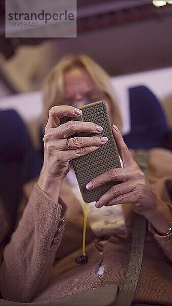 Nahaufnahme der Hände einer reifen Frau  die während einer Zugfahrt ein Smartphone benutzt  Weichzeichner