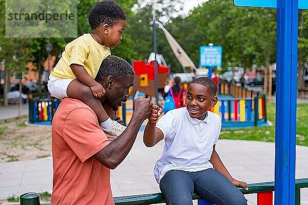 Afrikanischer schwarzer ethnischer Vater winkt mit seinen Kindern auf dem Spielplatz des Stadtparks
