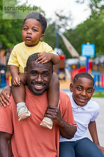 Porträt eines schwarzafrikanischen Vaters mit seinen Kindern auf dem Spielplatz des Stadtparks
